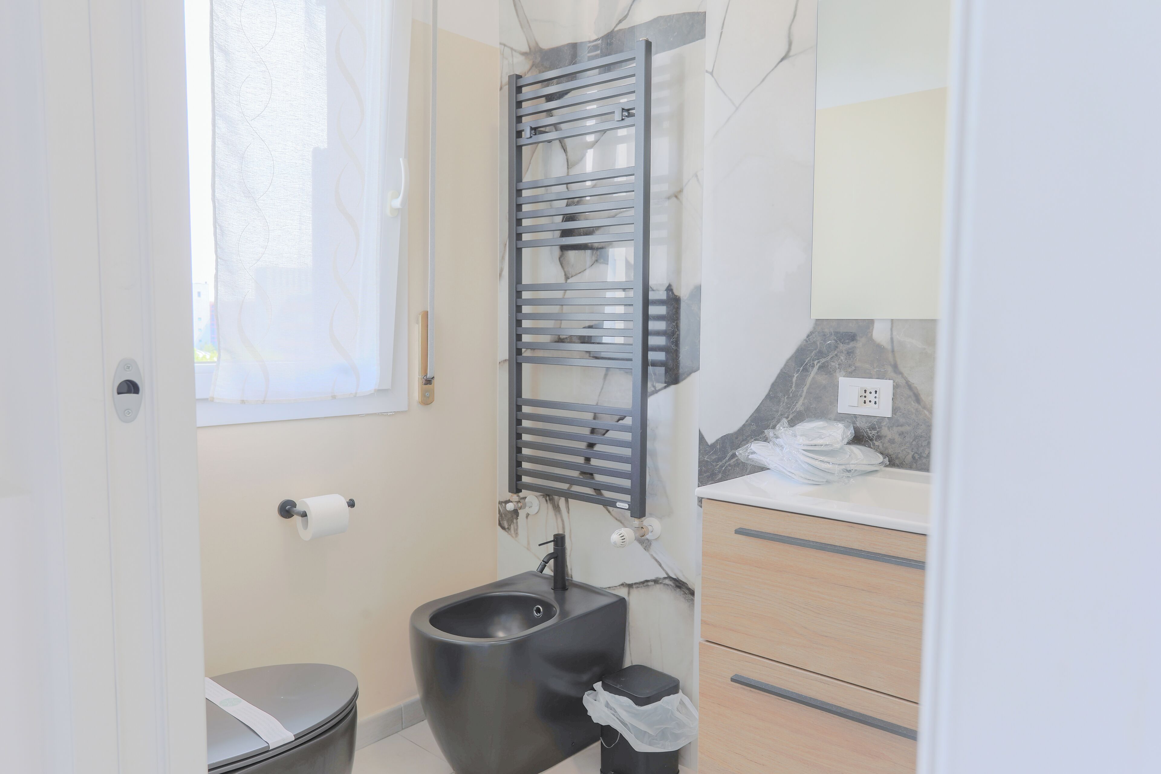 Een moderne badkamer met een zwart toiletbril, een handdoekhouder en een wastafel met een marmeren aanrechtblad.