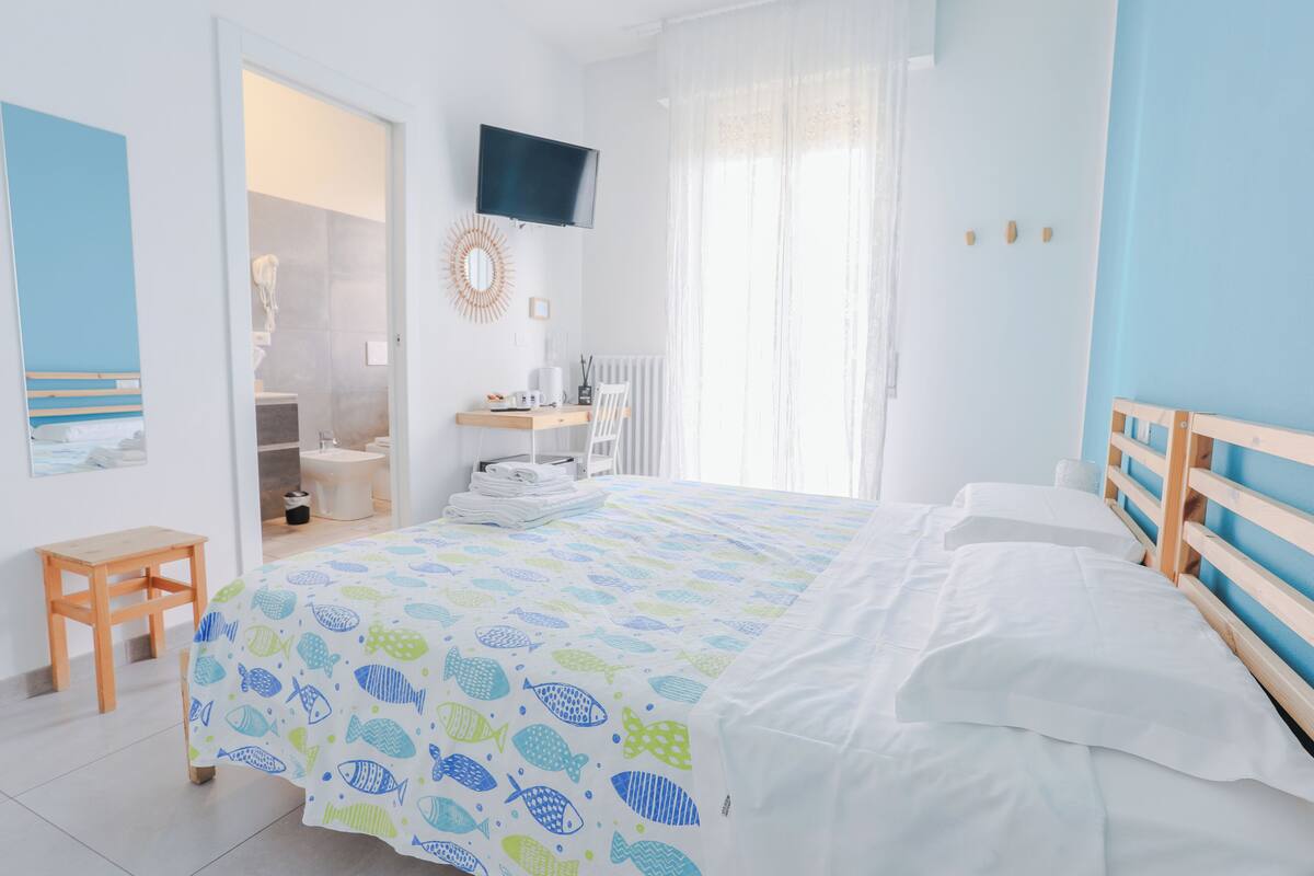 Un dormitorio con cama, televisión, baño y una pequeña mesa de madera.