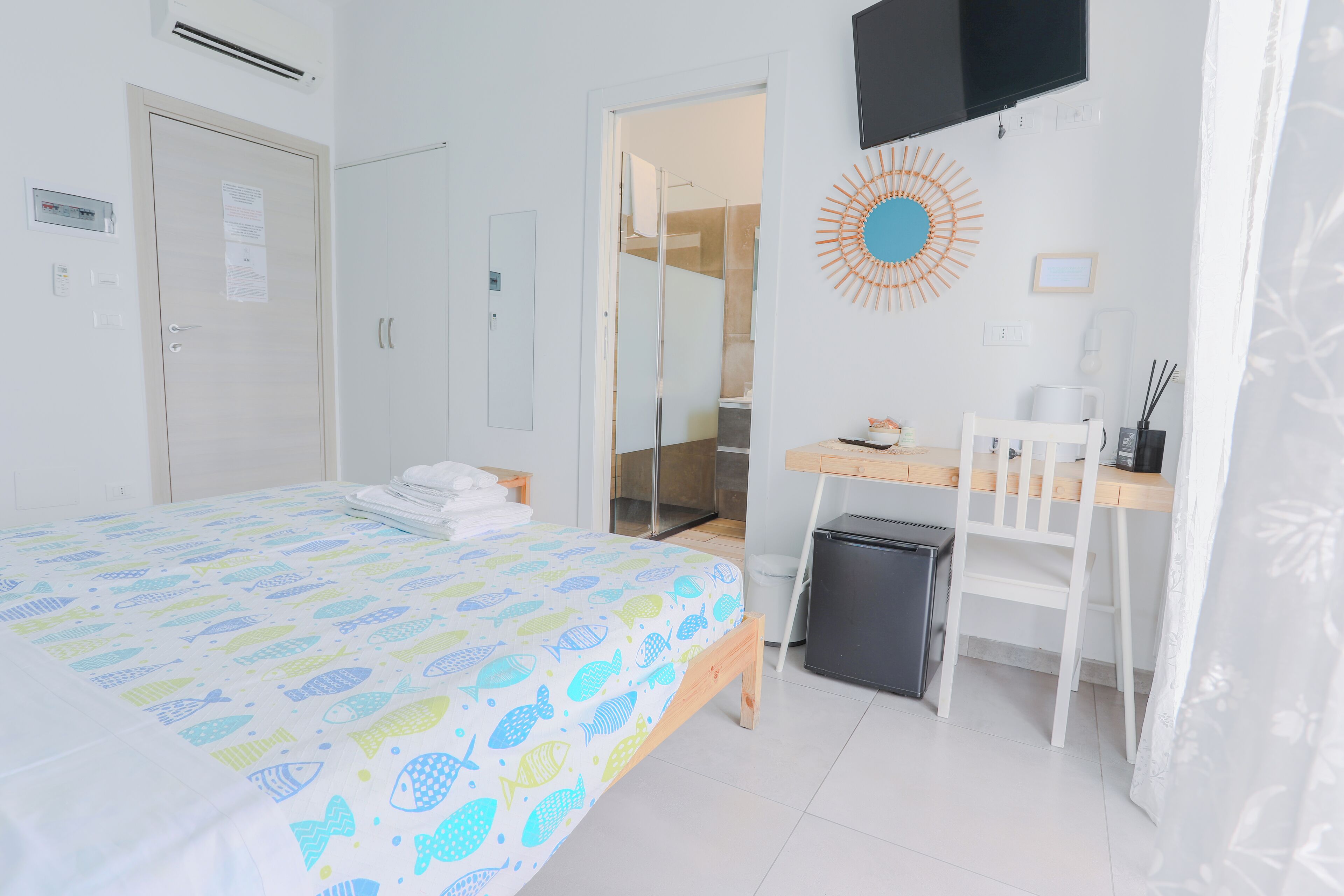 A hotel room with a bed, a desk, a chair, a TV, and a shower area.