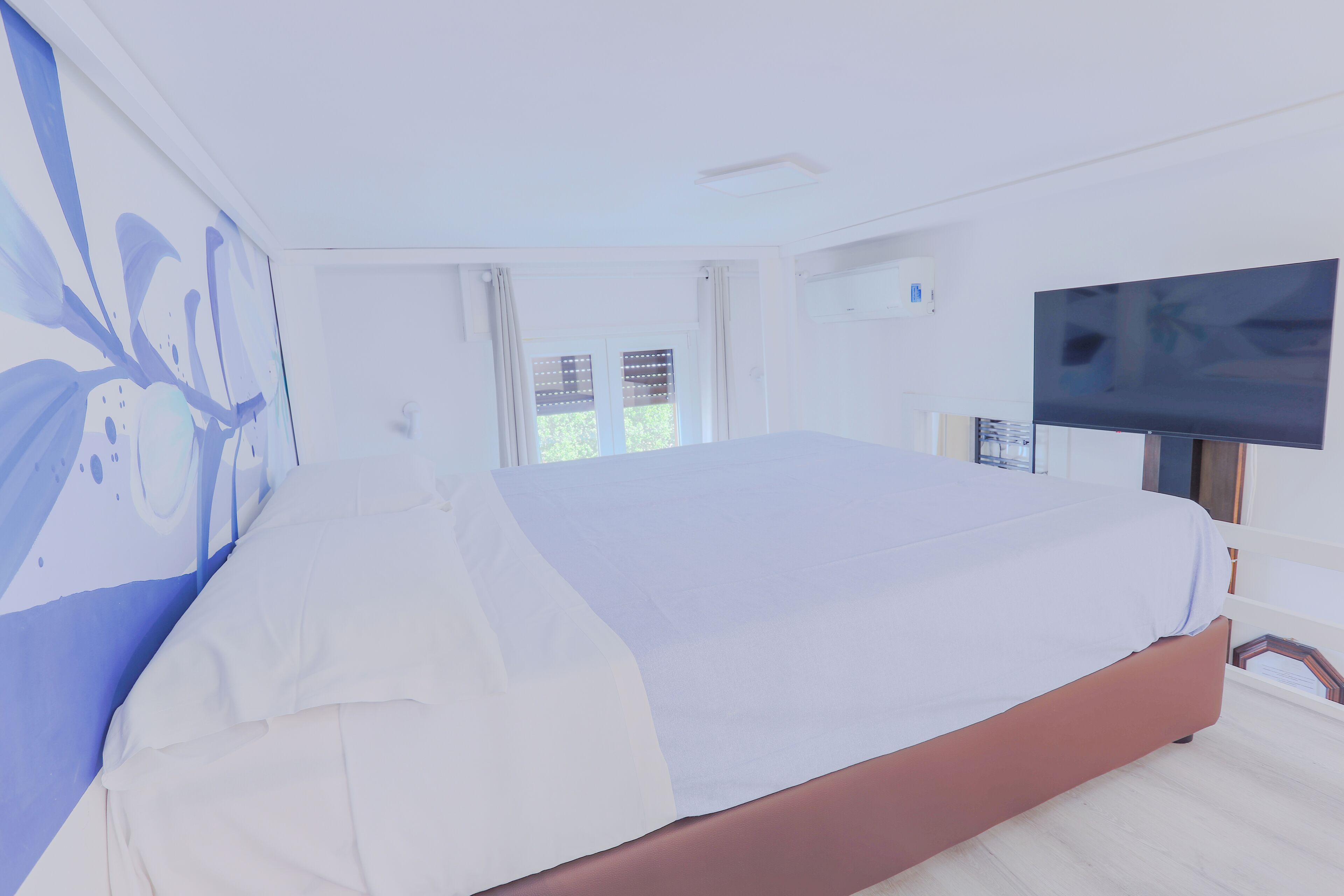 Une chambre à coucher avec un lit, une télévision et une fenêtre avec des rideaux.