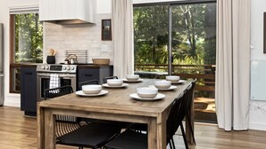A modern kitchen with a dining area, large windows, and a view of the outdoors.