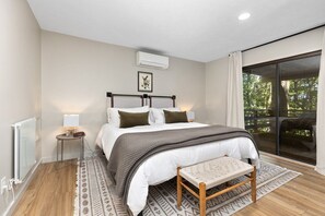 A bedroom with a bed, bedside table, bench, and a view of the outdoors.