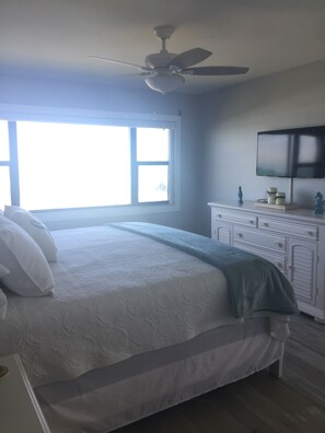A bedroom with a bed, a ceiling fan, a window, a dresser, and a television.