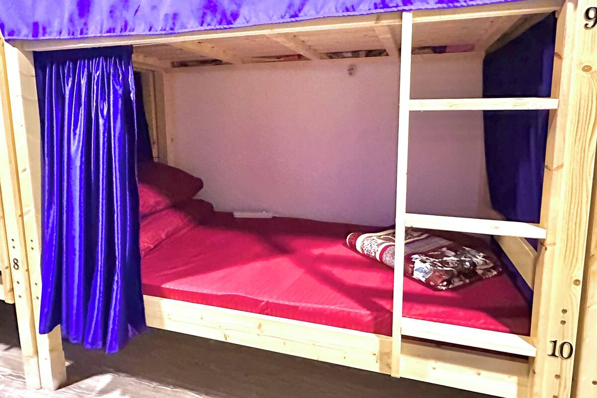 Ein Holzbett mit einer roten Matratze und blauen Vorhängen.