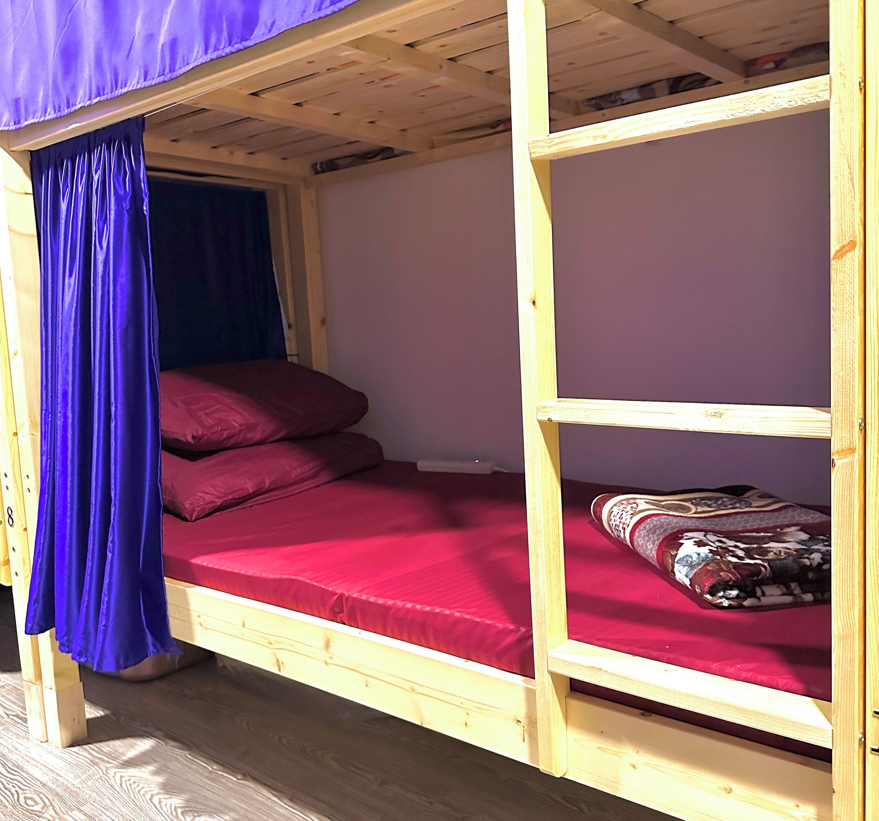 Ein Stockbett mit roter Matratze und Kissen, einem blauen Vorhang und einem Holzboden.