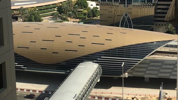 A modern building with a unique roof design, surrounded by a cityscape and a desert landscape. - Heartland Hostel (Dubai)