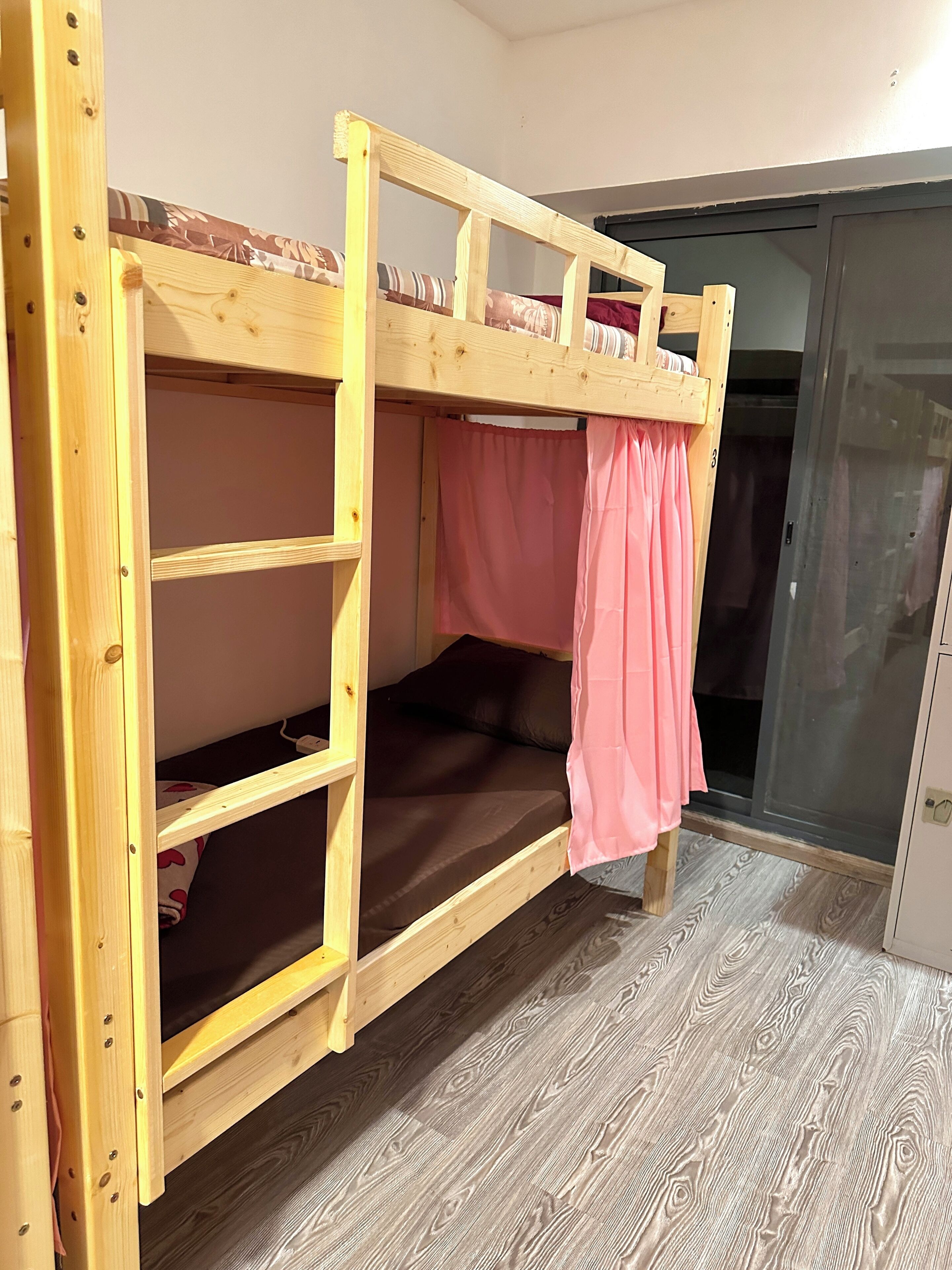 A bunk bed with a wooden frame, pink curtains, and a dark mattress.