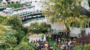 Cerimônia de casamento ao ar livre, com convidados sentados em cadeiras dispostas em fileiras, com vista para um porto com barcos e um cais.