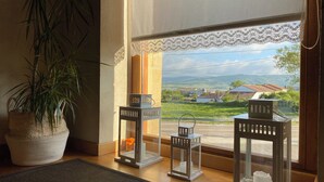 Ein Zimmer mit großem Fenster, einem Blumentopf und zwei weißen Laternen auf Holzboden.