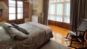 Ein Schlafzimmer mit einem großen Bett, einem hölzernen Schaukelstuhl, einer Chandelüster und einem Kamin aus Stein.
