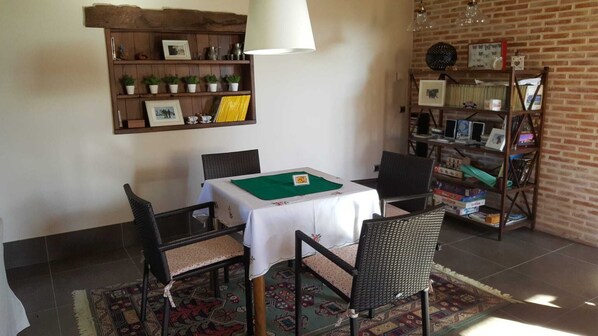 Un coin repas avec une table dressée pour quatre personnes, entourée de chaises en osier, d’un tapis à motifs et d’une bibliothèque contenant divers objets.