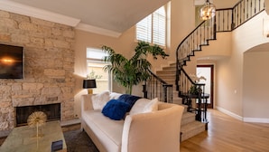 A spacious living room with a stone fireplace, a large potted plant, and a staircase leading to an upper level. - Guarded gated community right across the street from the Waldorf Astoria (Dana Point)