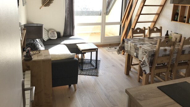 Un espacio de estar acogedor con sofá, una mesita, una mesa de comedor con sillas, una escalera y vistas al exterior.