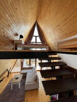 A cozy attic bedroom with wooden walls, a bunk bed, a sofa, and a dining table.