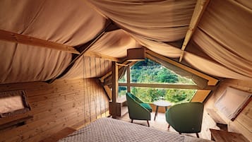 Alojamiento tipo tienda de campaña con cama, dos sillas y ventana con vistas a la vegetación.