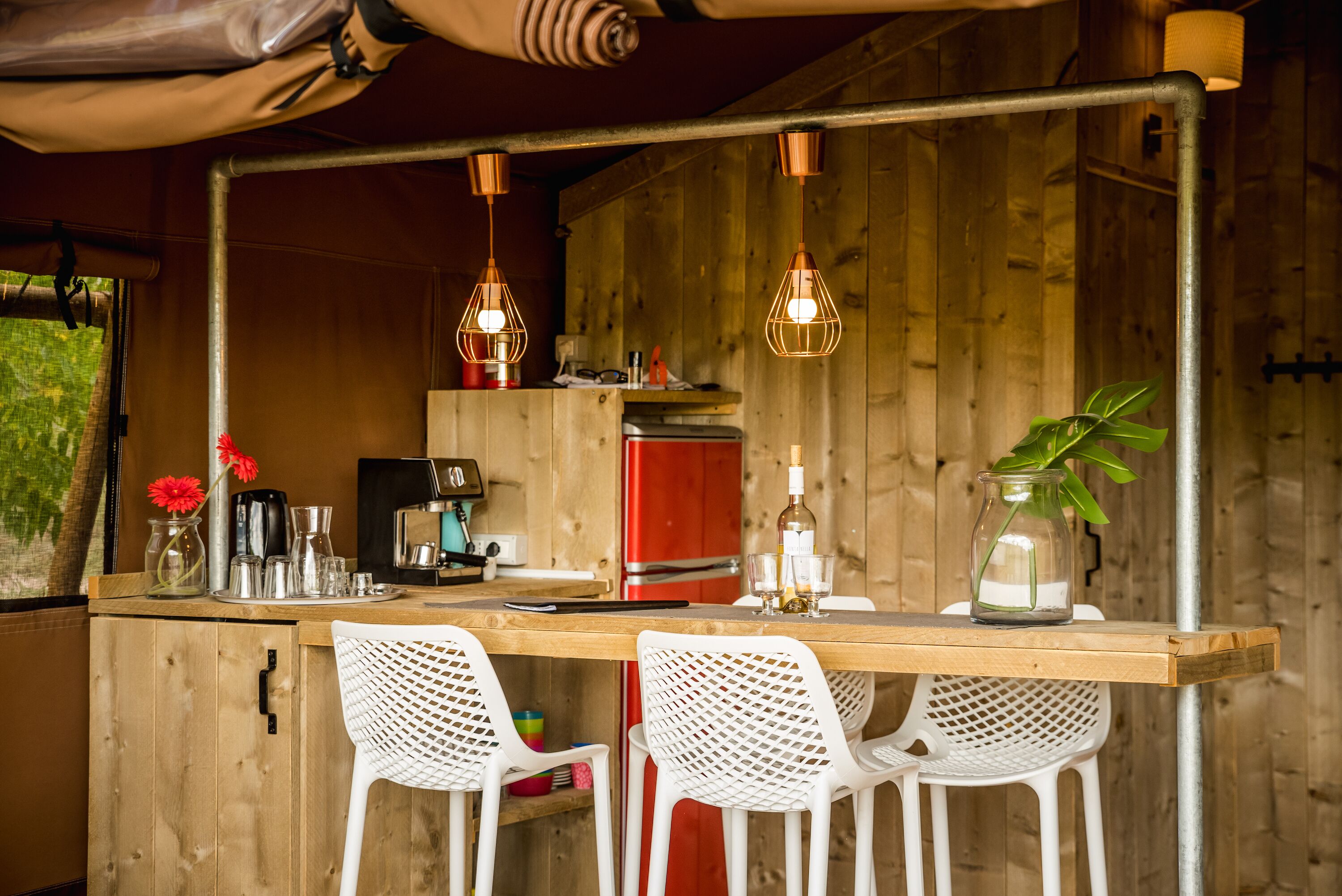 A rustic wooden kitchen with a bar area, white chairs, and hanging pendant lights.
