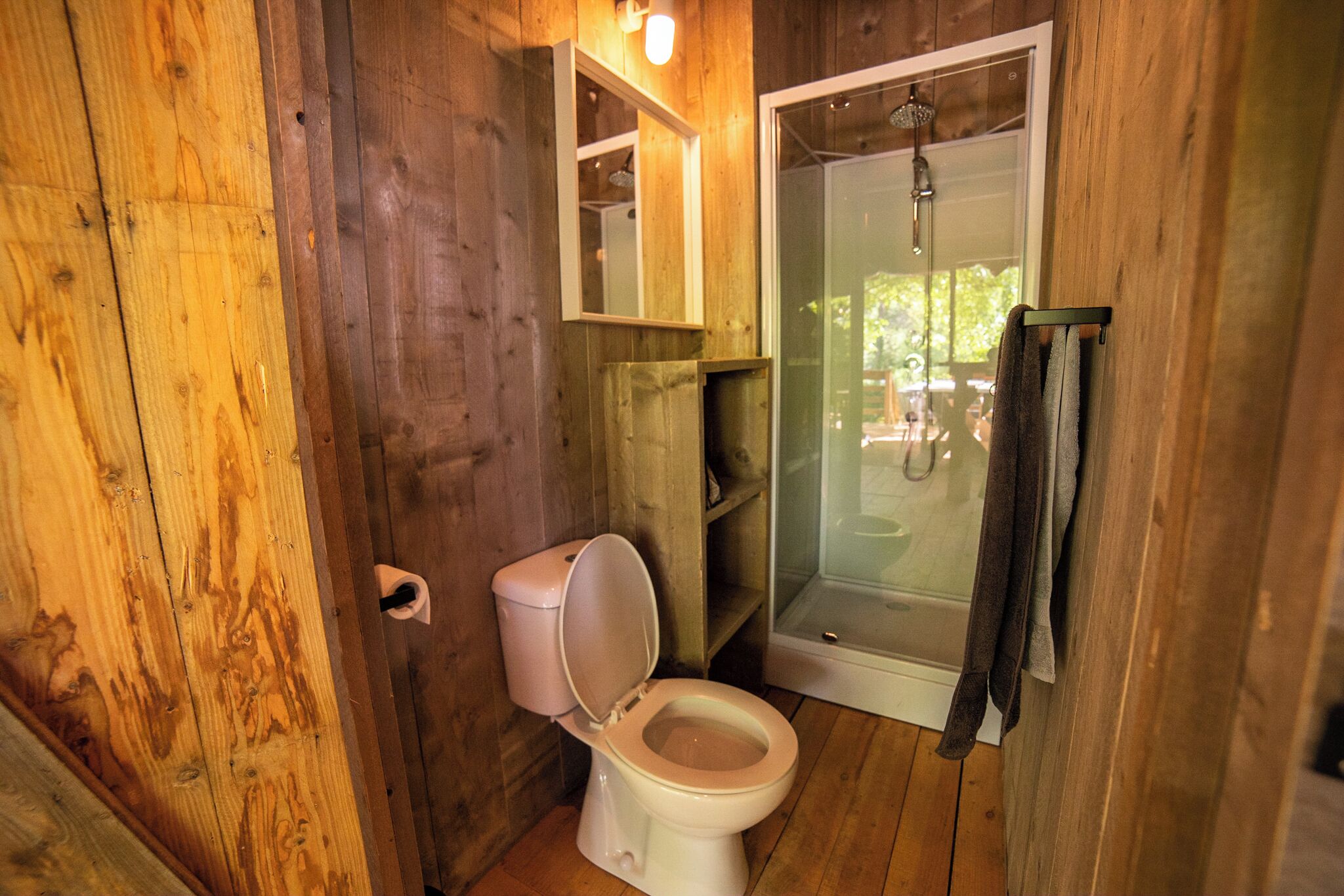 A wooden bathroom with a toilet, a glass shower enclosure, and a towel rack.