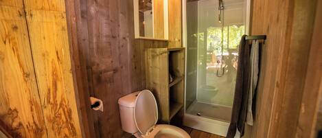 A wooden bathroom with a toilet, a glass shower enclosure, and a towel rack.