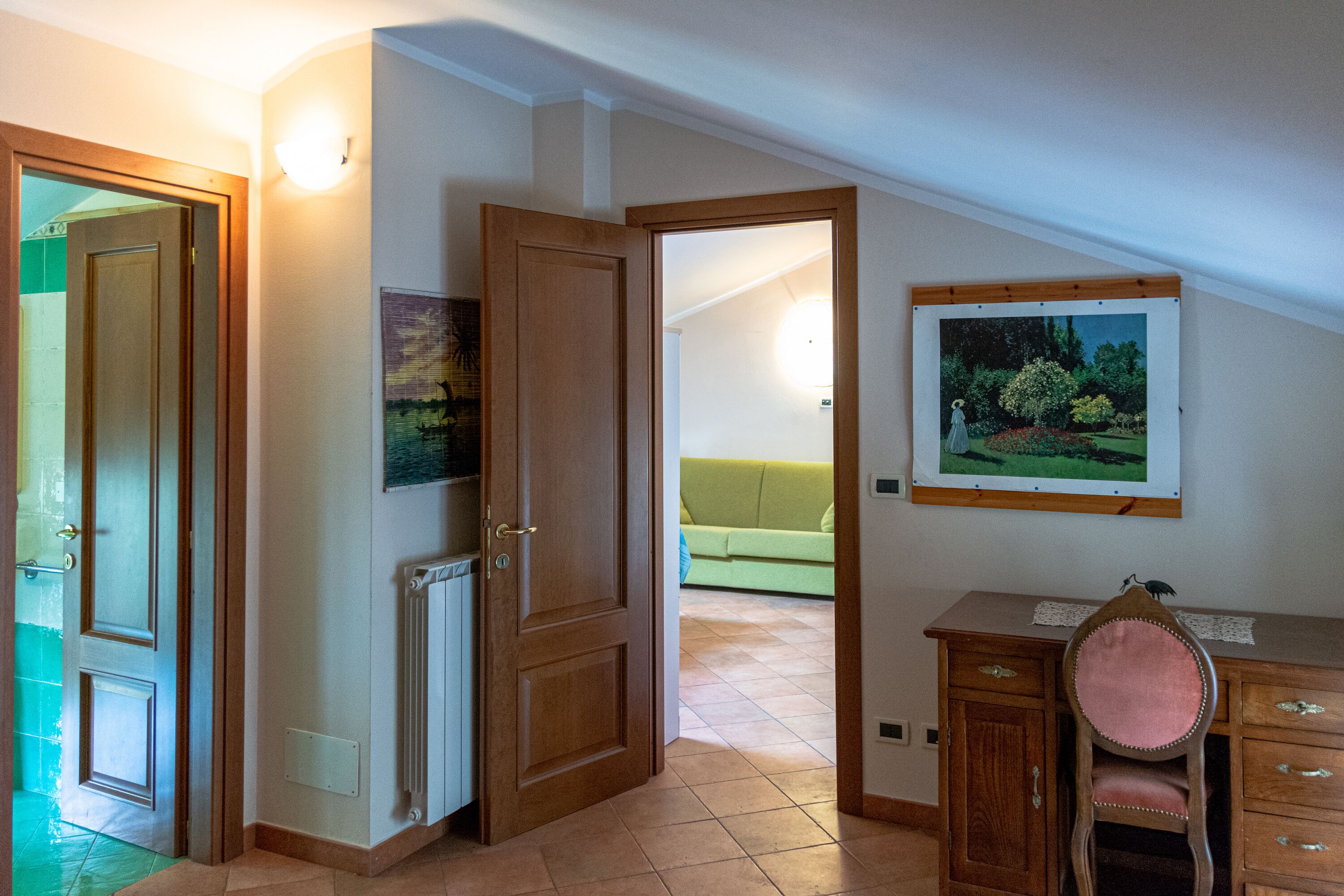 Une pièce avec une porte en bois, un radiateur, un canapé vert et un bureau avec une chaise.