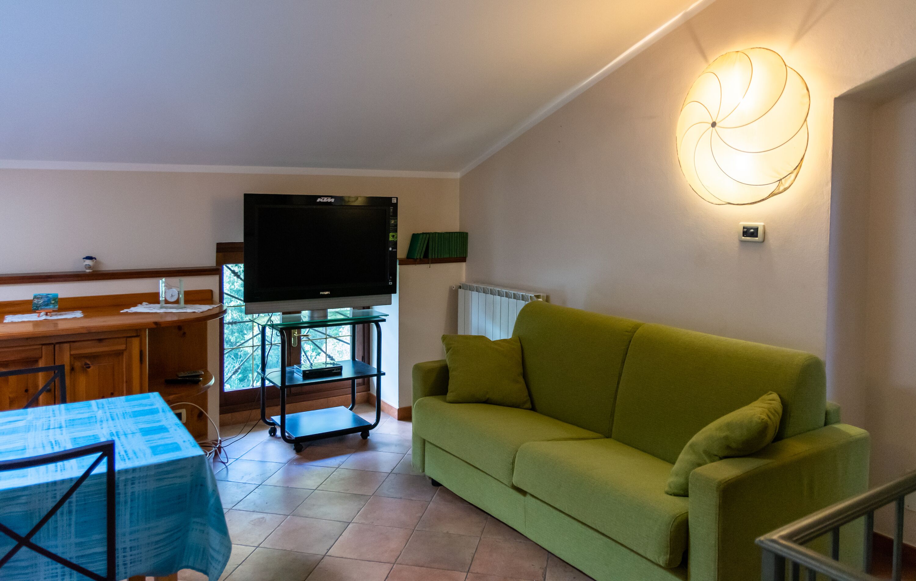 A living room with a green sofa, a TV, a wooden table, and a glass cabinet.