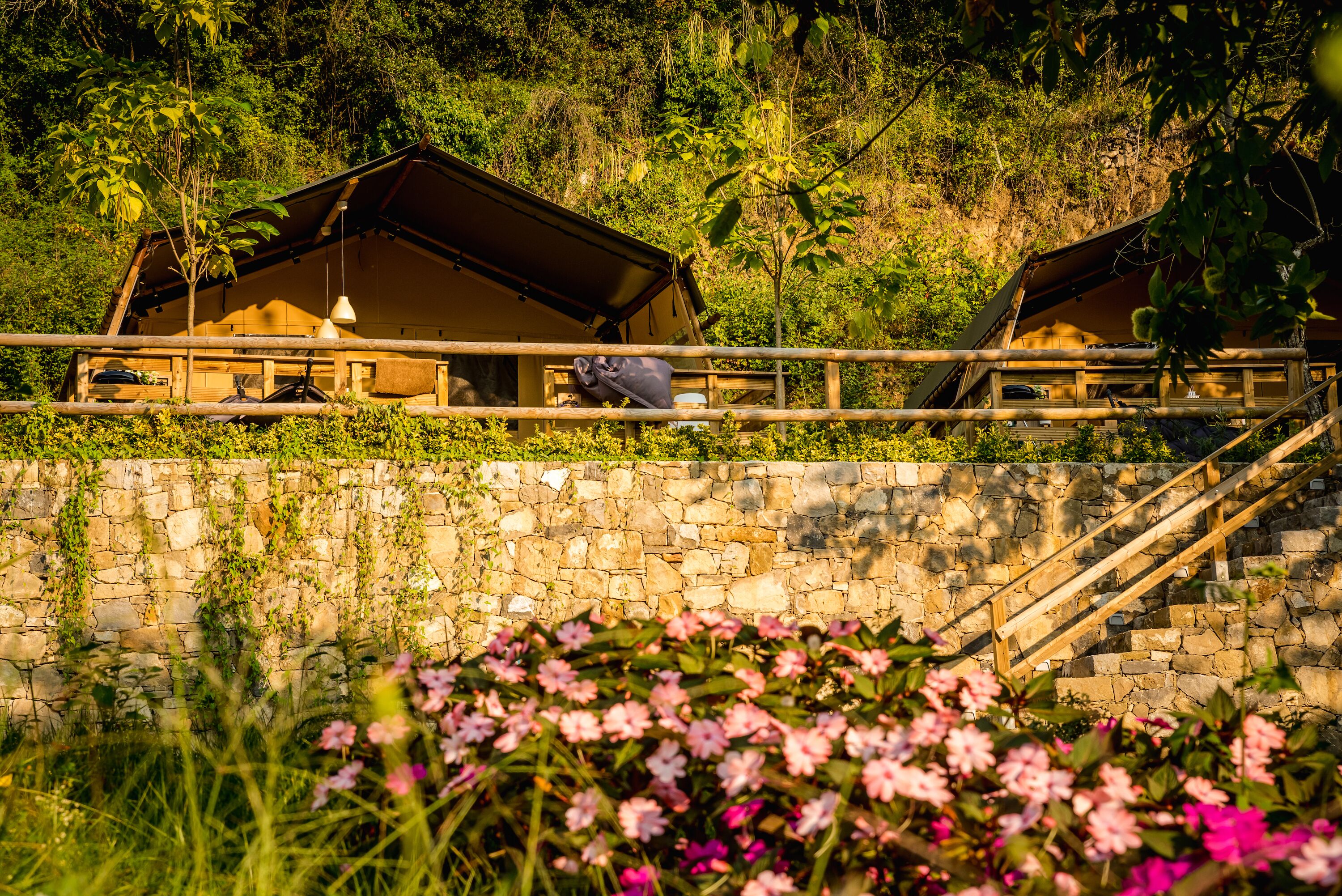 A rustic wooden cabin with a stone wall and a wooden staircase leading up to it.