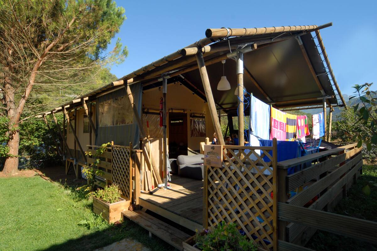 Une cabane en bois rustique dotée d’un porche couvert, d’un petit coin salon et d’un espace buanderie où le linge est étendu.