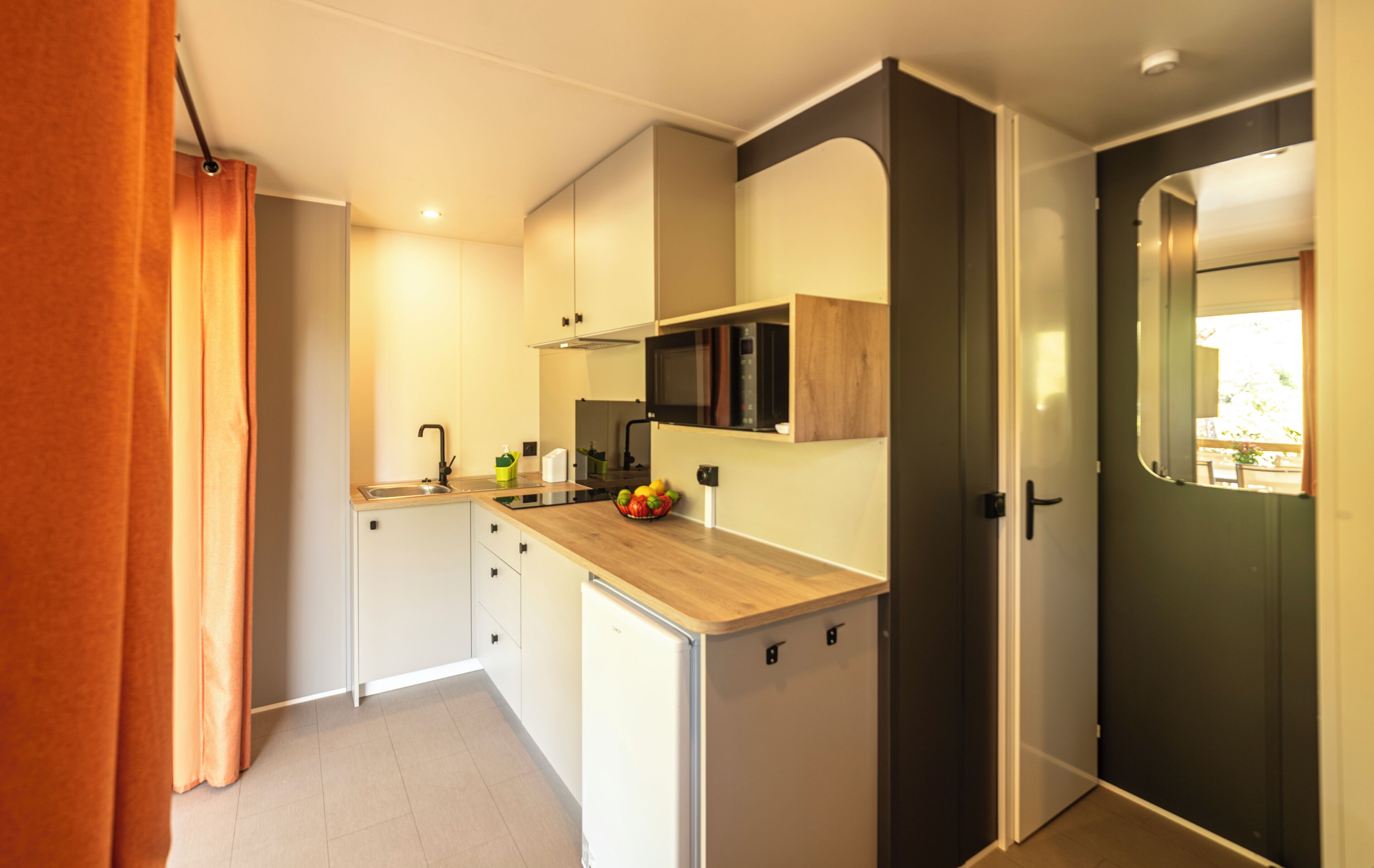 A compact kitchen with a microwave, sink, and a fruit bowl on the counter.