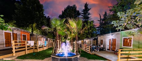 A courtyard with a central fountain, wooden deck, and spa-like cabins.
