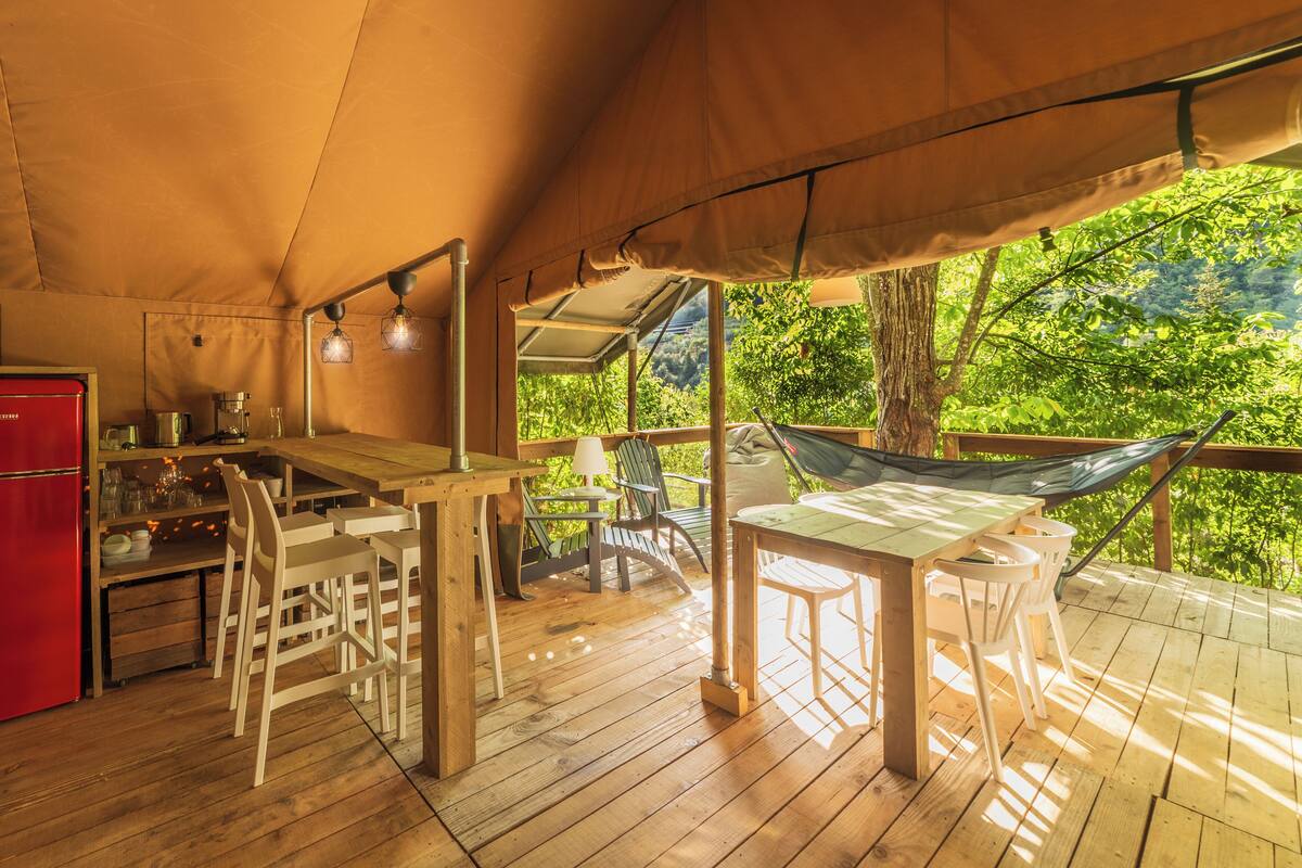Une terrasse en bois avec une table à manger, des chaises, un hamac et un réfrigérateur rouge.