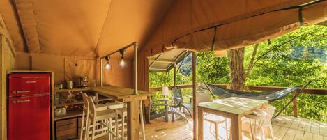 Eine Holterrasse mit Esstisch, Stühlen, einer Hängematte und einem roten Kühlschrank.