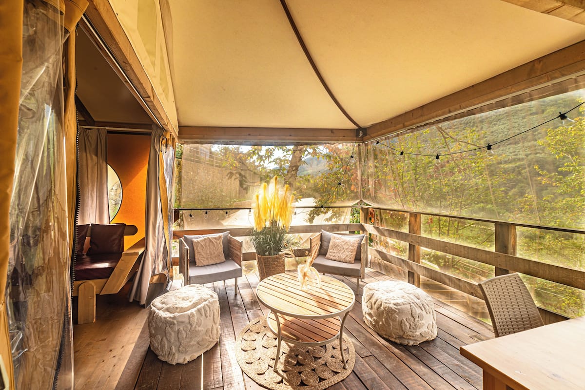 Une terrasse extérieure avec des meubles en bois, une table ronde et une vue sur la forêt environnante.