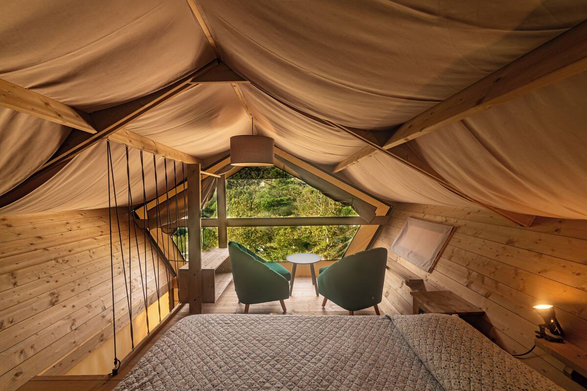 Une chambre confortable située dans les combles, avec un lit, deux fauteuils, une petite table et une vue sur la verdure.
