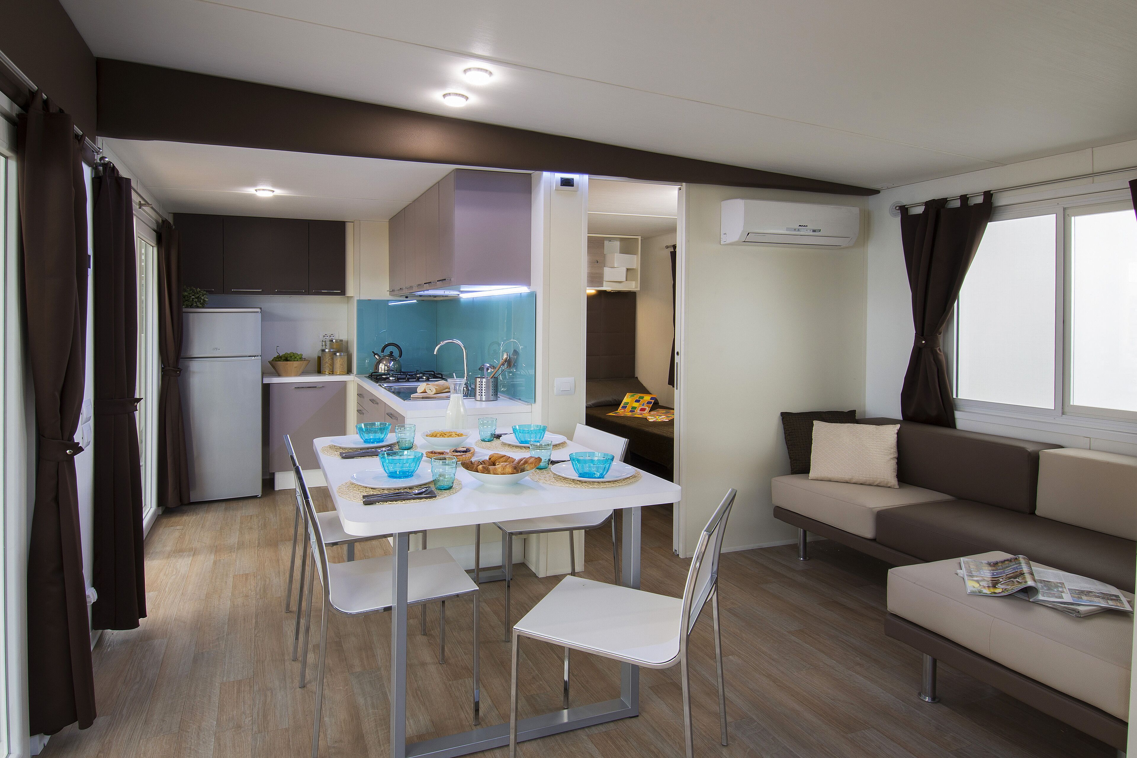 Una cocina moderna con armarios blancos, una mesa de comedor con sillas y un sofá en la sala de estar.