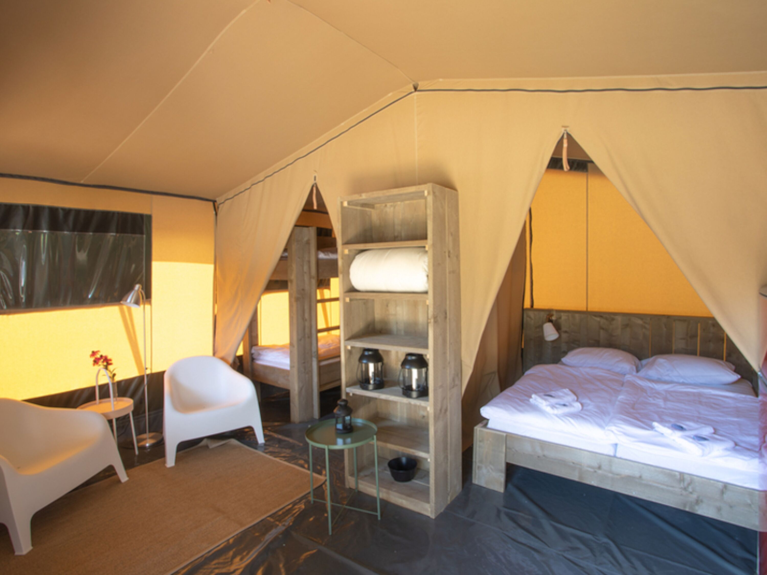 Habitación tipo tienda de campaña con una cama, una silla, una mesita y una estantería con objetos.