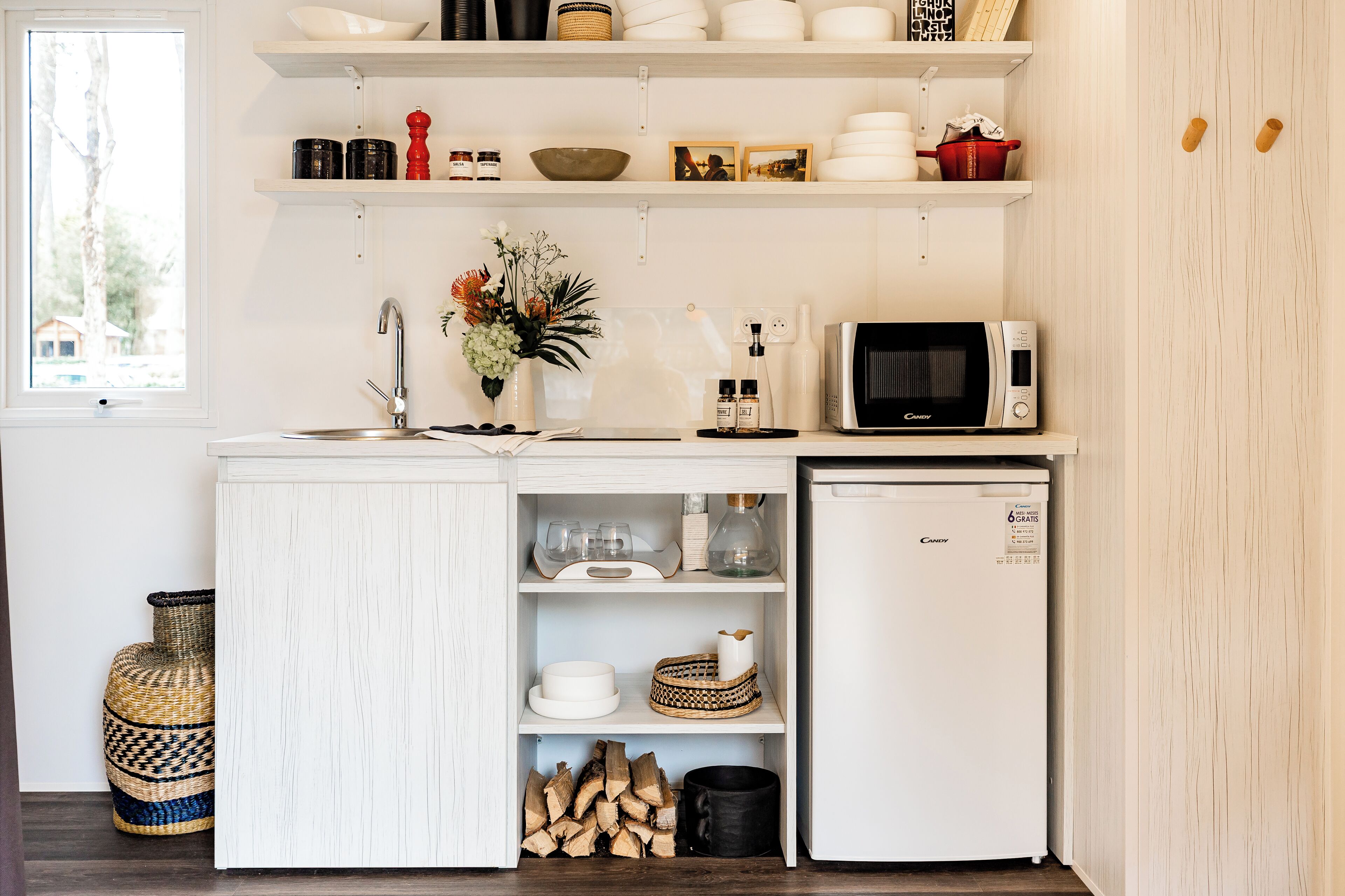 A compact kitchen with white cabinetry, a microwave, a refrigerator, and shelves with various kitchen items.