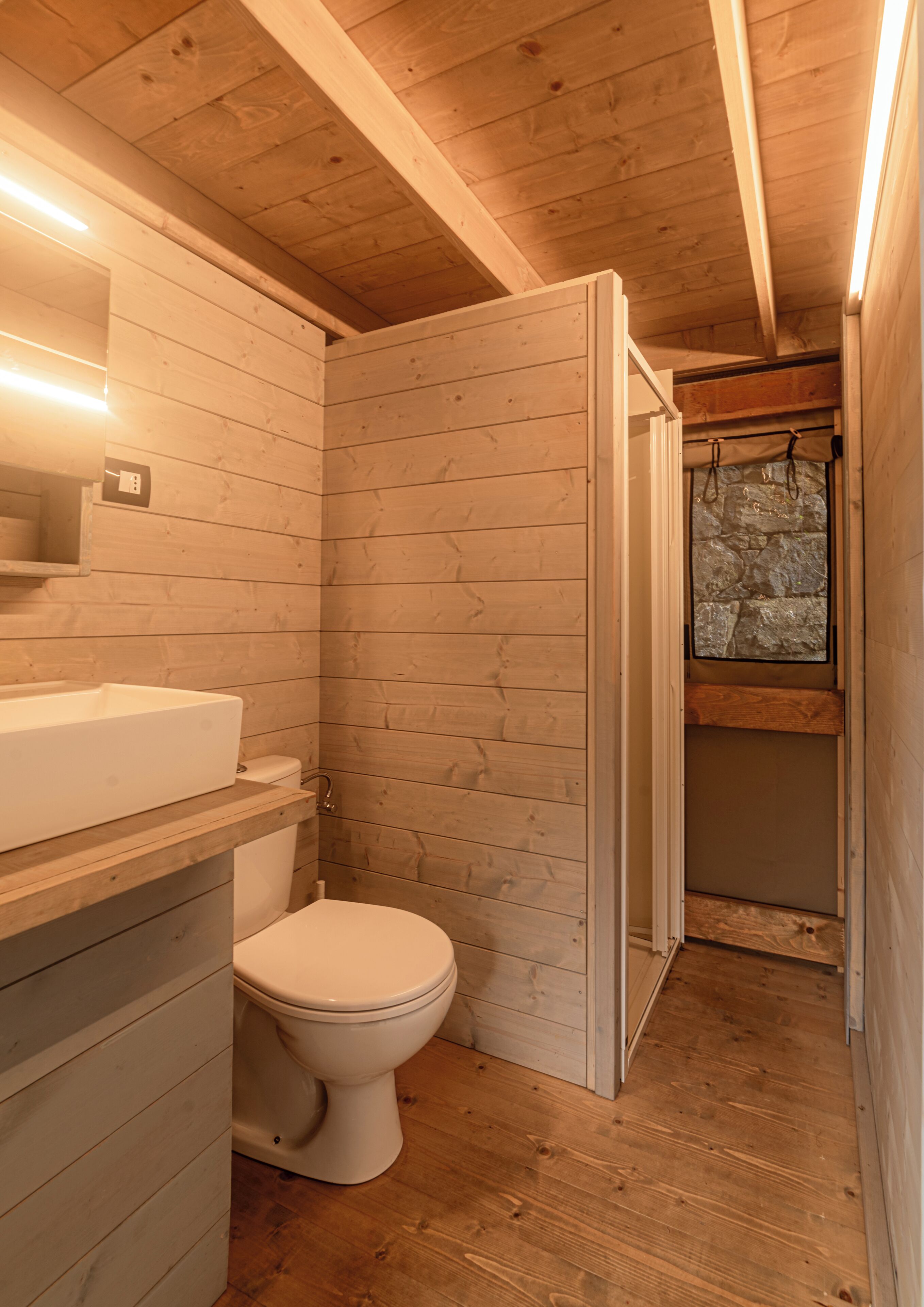 A wooden-paneled bathroom with a toilet, sink, and shower area.
