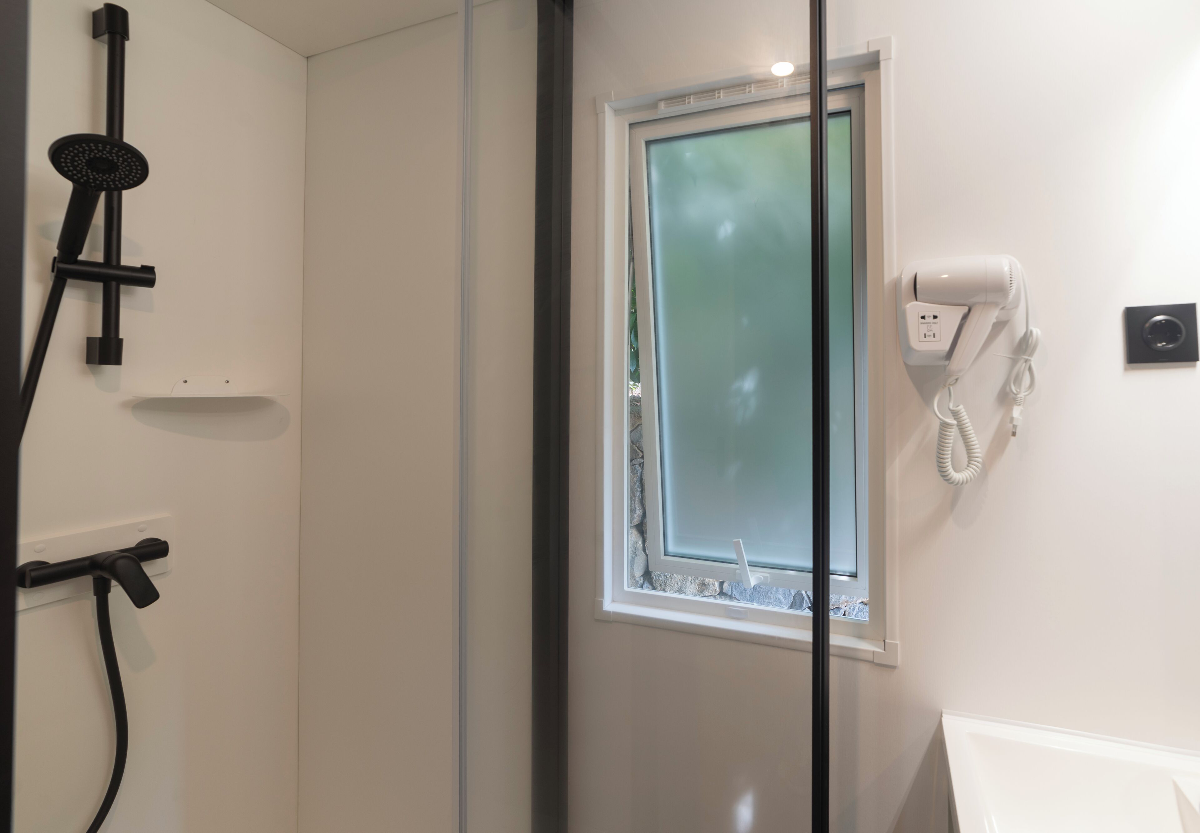 Un baño con ducha, una ventana y un secador de pelo en la pared.