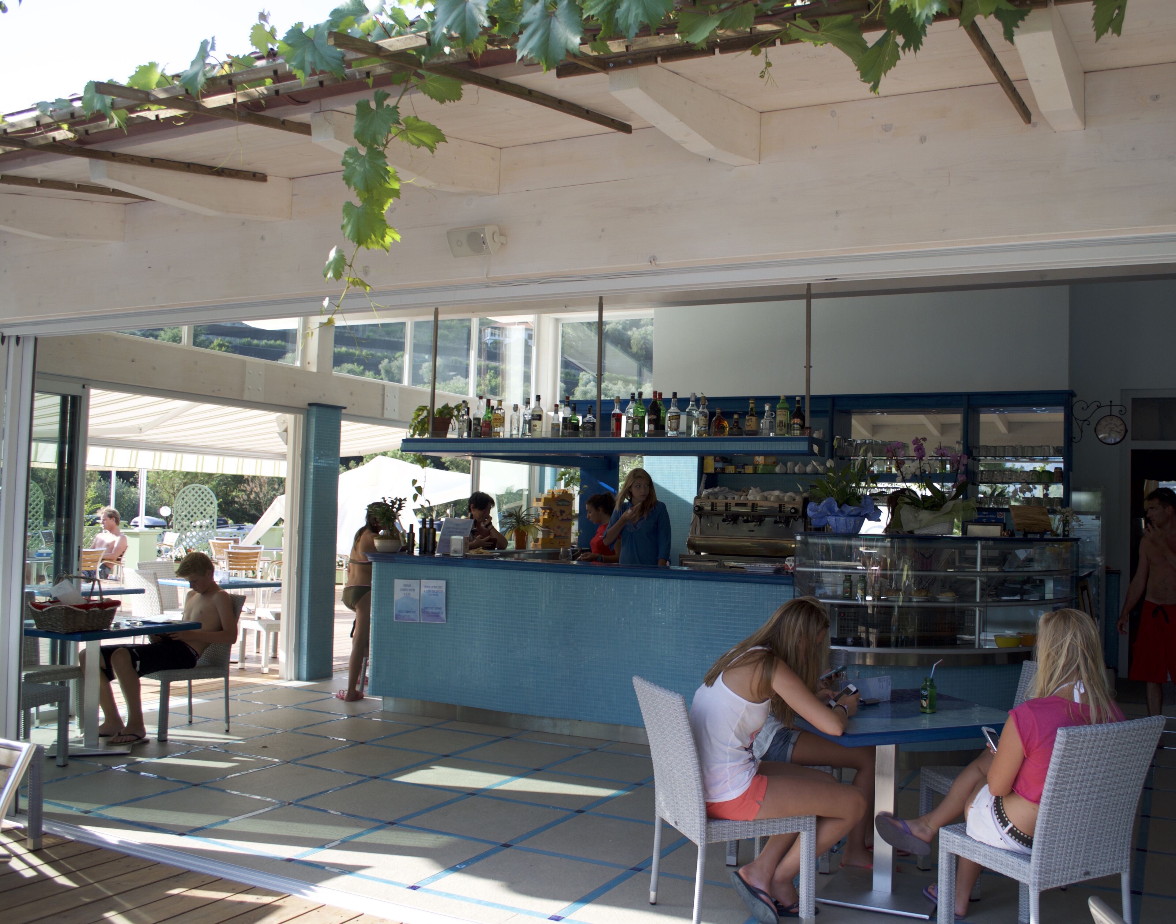 Zona de bar al aire libre con mostrador, asientos y vistas del exterior.