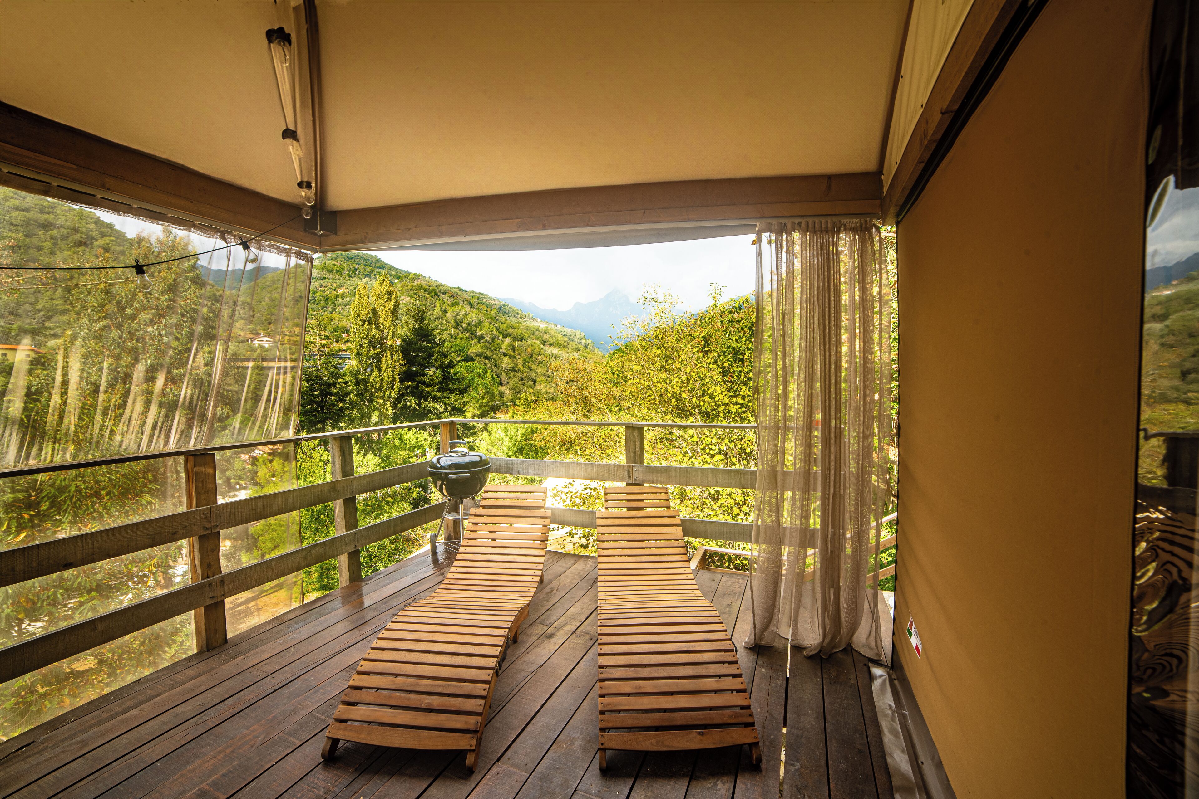 Une terrasse en bois avec deux chaises longues et un barbecue, offrant une vue sur un paysage montagneux.