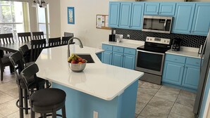 A modern kitchen with blue cabinets, a white countertop, and a central island with a fruit bowl.