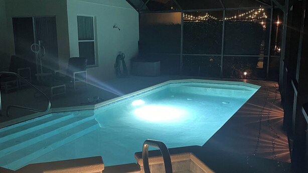An indoor swimming pool with a clear water surface, surrounded by a covered area with seating and a view of the outdoors.