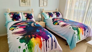 A bedroom with two beds, each with colorful, abstract bedspreads. There are two bedside tables with lamps, and the room has light blue walls.
