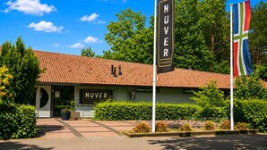 Rakennuksessa on tiilikatto, kyltti, jossa lukee ”NUVER”, ja kaksi lippua.