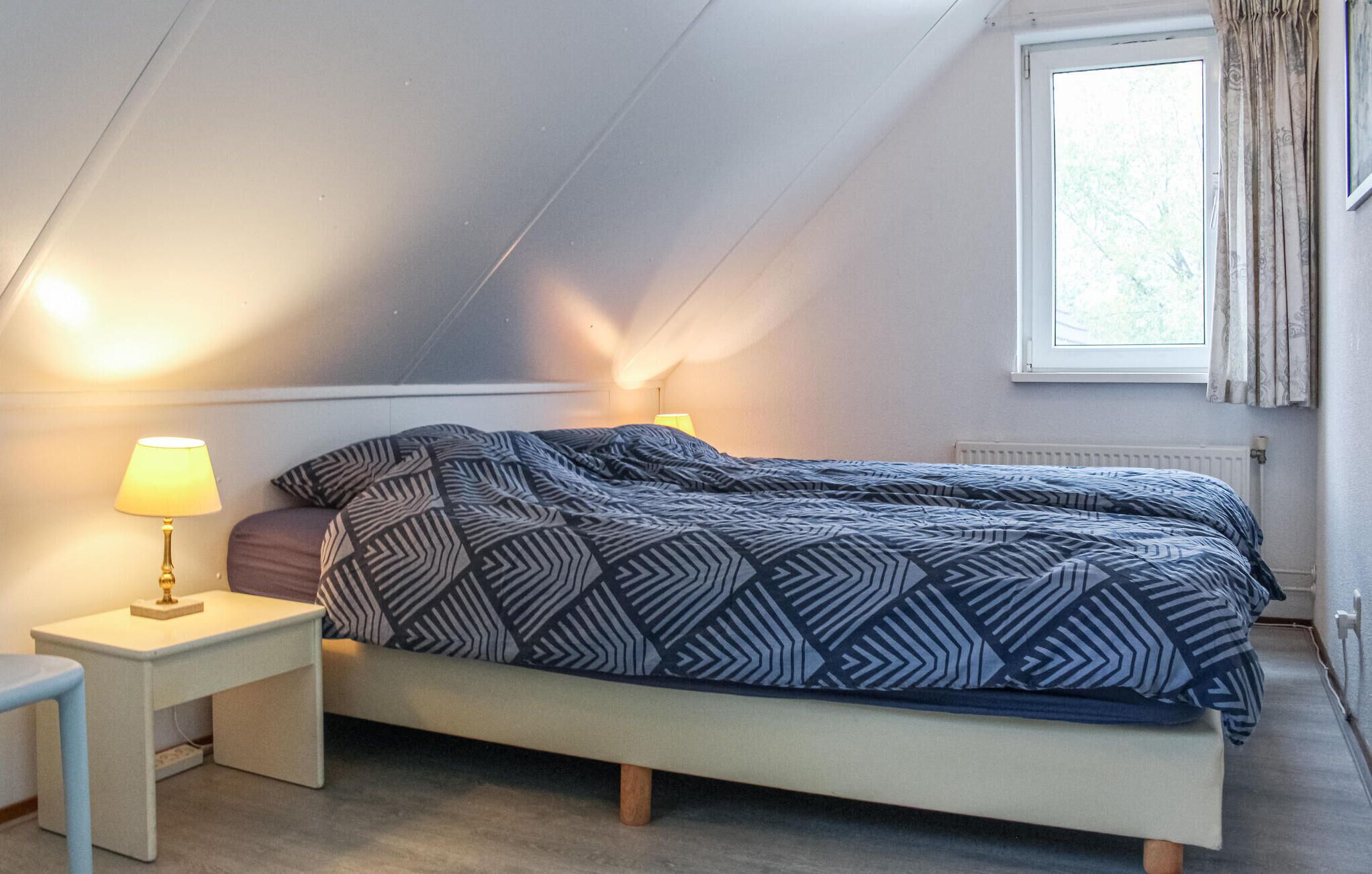 Une chambre à coucher avec un lit, des lampes de chevet, une fenêtre et un radiateur.