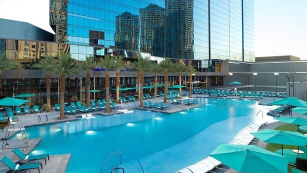 A large indoor swimming pool with multiple lanes, surrounded by lounge chairs and umbrellas, and a modern building with reflective glass windows in the background. - Perfect for Conferencing, Shopping, Dining, Shows and the Strip! (Las Vegas)