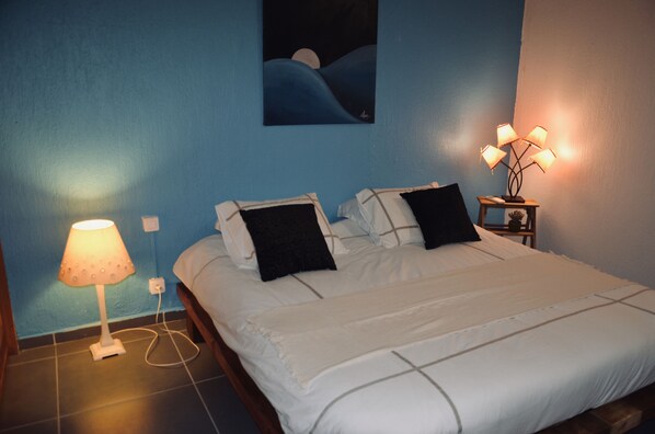 A bedroom with a bed, two bedside lamps, a wall painting, and a nightstand with a lamp. - Cosy loft Bas du Fort (Le Gosier)