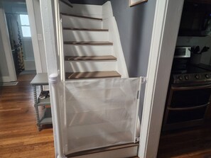 Una escalera con escalones de madera y barandilla blanca, que lleva a una zona de cocina con estufa y horno.