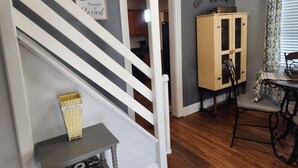 Una escala amb baranes blanques que porta a una cuina amb armaris de fusta i una taula de dinar.