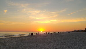 A beach with people walking and standing, and a sunset in the background. - Super Nice Quiet Beach Cottage, Pvt Parking, WiFi, Cozy, Spotless, Comfortable.  (Gulf Shores)