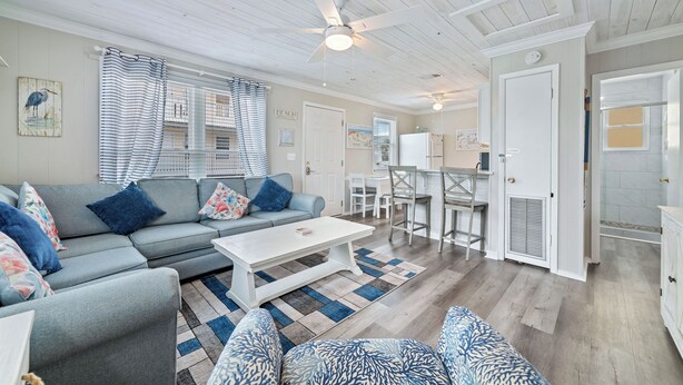 A spacious living room with a grey sofa, a white coffee table, and a striped curtain. - Super Nice Quiet Beach Cottage, Pvt Parking, WiFi, Cozy, Spotless, Comfortable.  (Gulf Shores)